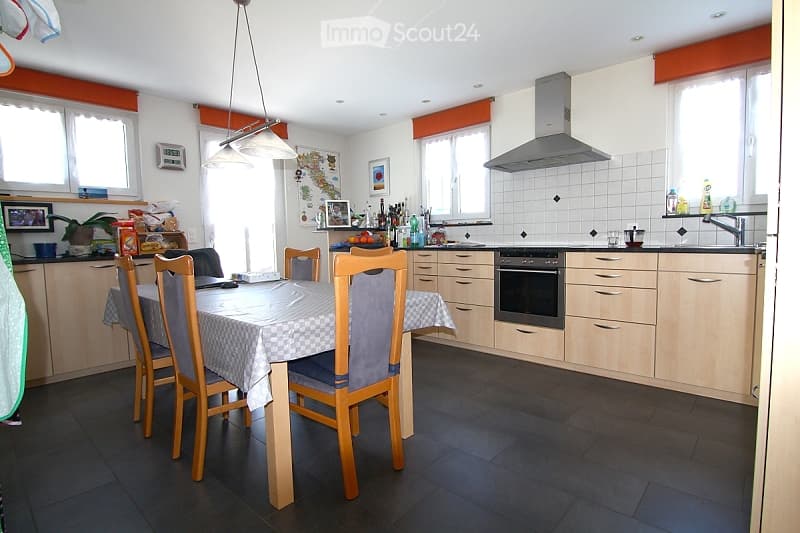 Bright kitchen with light wooden cabinets, a dining area with a table and chairs, and various appliances including an oven and a sink.