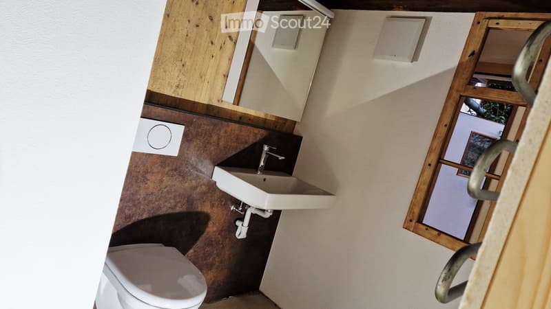 Compact bathroom with a toilet, sink, and faucet. The walls are painted in a neutral tone with wooden trim around the window and cabinetry.