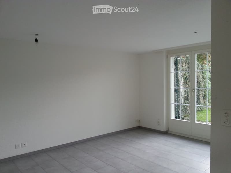 Empty room with white walls, tiled floor, and a large window with white frame, allowing natural light to enter.