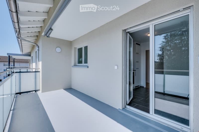 Modern balcony with glass sliding doors, white walls, and a view of the surrounding area.