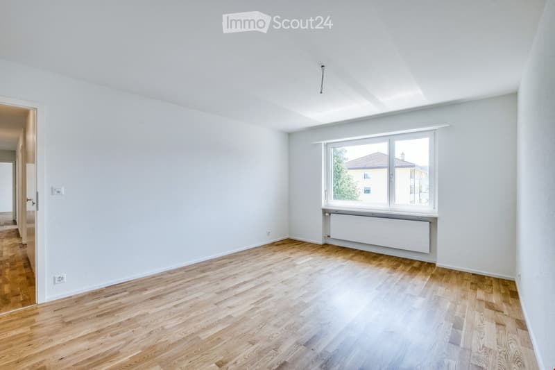 Empty room with light-colored wooden flooring, white walls, and a large window with a radiator below it. No furniture or equipment is present.