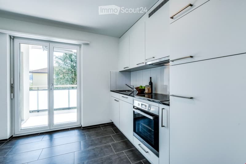 Modern kitchen with white cabinets, stainless steel appliances, dark tiled floor, and a sliding glass door leading to a balcony.