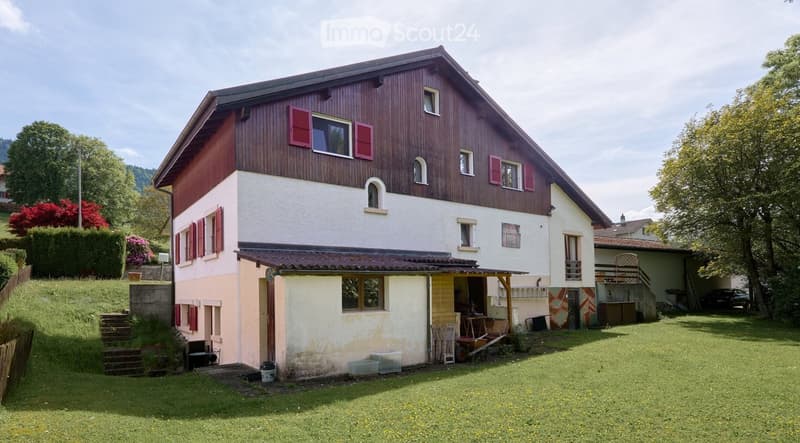 Two-story house with red shutters and a wooden facade, surrounded by a well-maintained lawn and garden area.