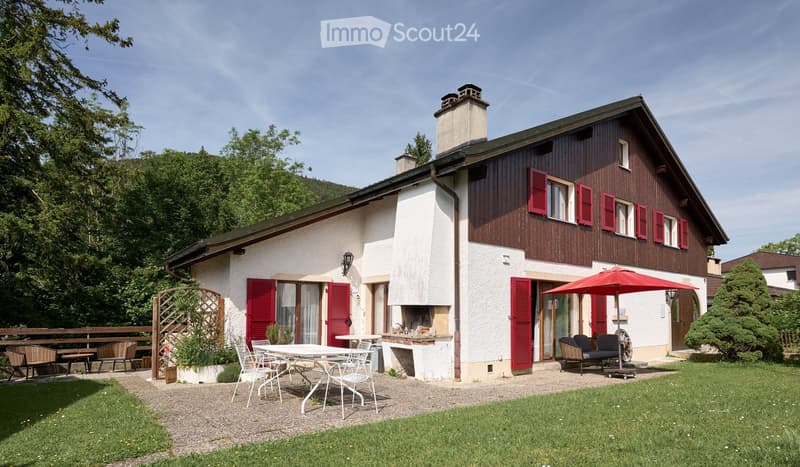 Two-story house with red shutters, white walls, and a wooden facade. Features include a patio with outdoor furniture, a fireplace, and a garden area.