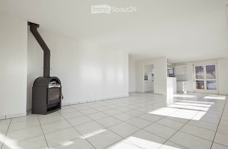 Empty room with white tiled floor, white walls, and a black wood-burning stove with a chimney. No furniture or equipment present.