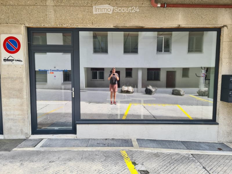 Building entrance with glass doors, a no-parking sign, and a reflection of a parking area with rocks and a person in the glass.