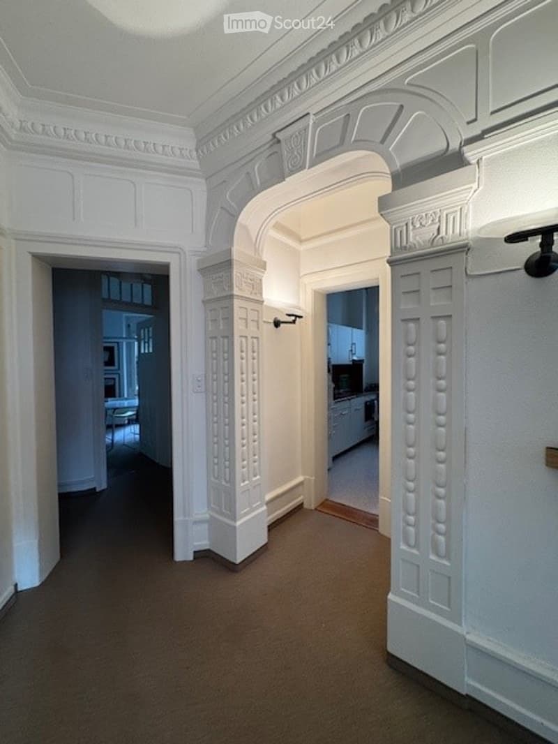 Elegant hallway with white decorative molding, arched entryway, and visible rooms on either side.