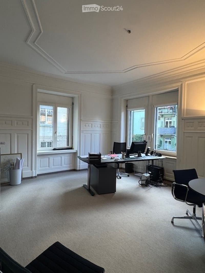Office space with a large desk, computer, chairs, and large windows with blinds.