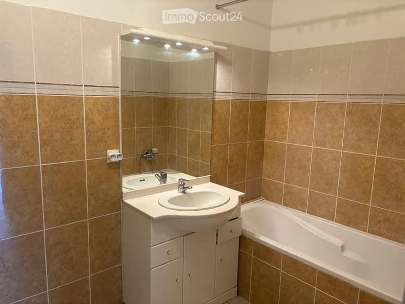 Modern bathroom with a white vanity, sink, mirror with LED lighting, and a bathtub.