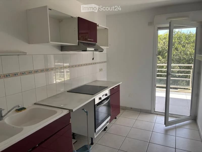 Modern kitchen with white tiled walls, dark red cabinets, induction cooktop, oven, and a sink. An open sliding door leads to a balcony.