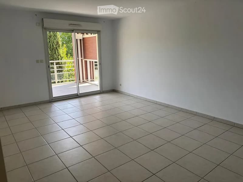 Empty room with tiled floor, white walls, and a sliding glass door leading to a balcony.