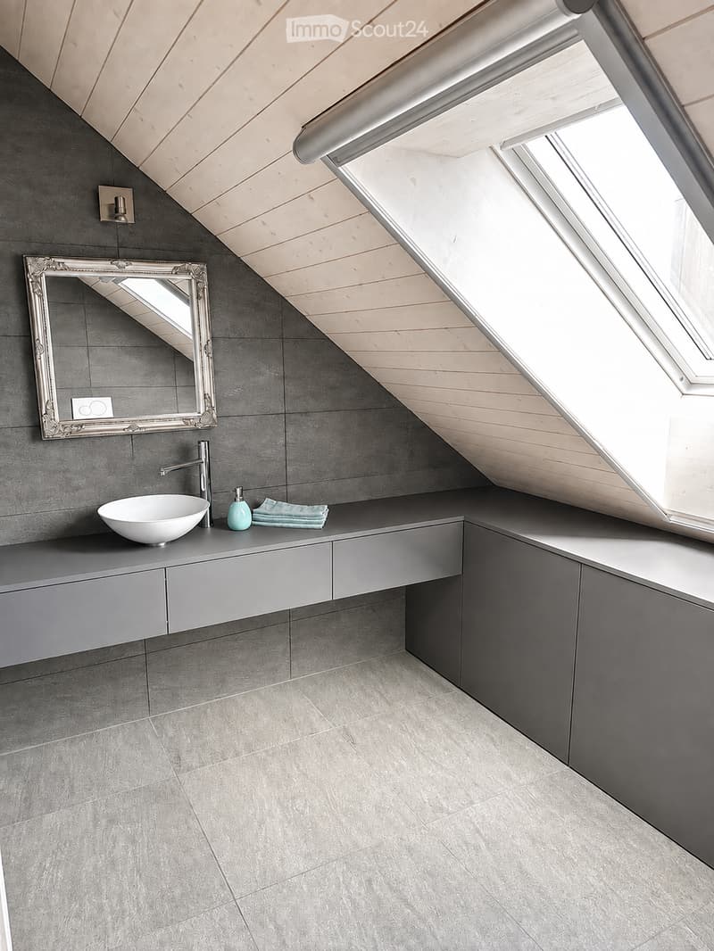 Modern bathroom with grey tiles, a sleek sink, a decorative mirror, and a skylight window allowing natural light.