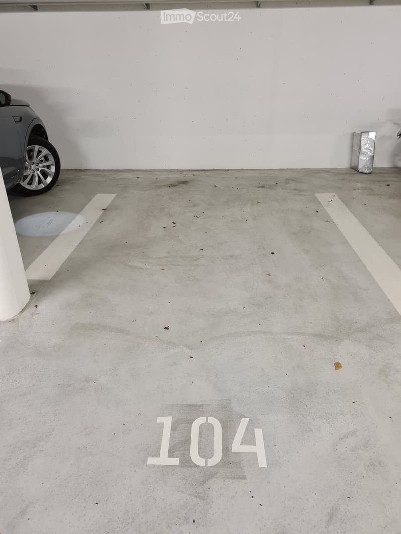 Parking lot with number 104, white walls, clean floor, parked car, silver object