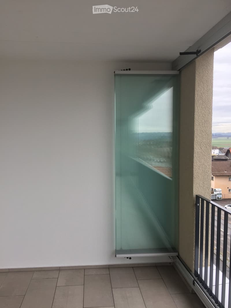 Balcony with tiled floor, glass sliding door, metal railing, and view of the surrounding area.