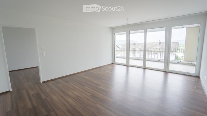 Empty room with wooden flooring, white walls, and large sliding glass doors leading to a balcony.
