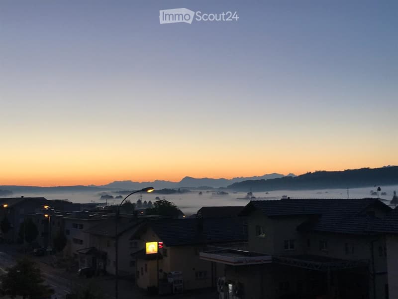View of a town at sunrise with houses, a gas station, and distant mountains shrouded in mist.