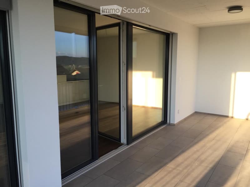 Spacious balcony with large glass sliding doors, tiled floor, and a scenic city view.