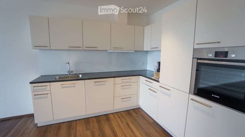 Modern kitchen with white cabinets, black countertops, and a stainless steel oven. Features a wooden floor and a sleek design.