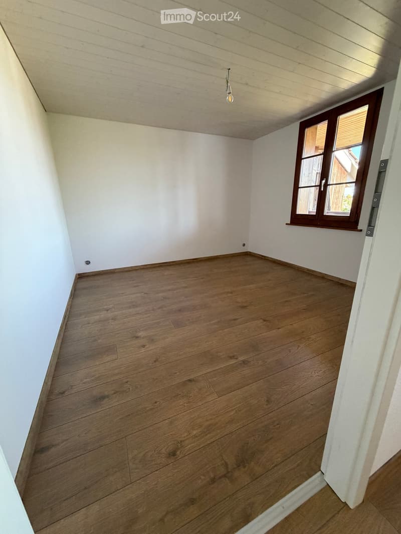 Empty room with wooden flooring and white walls, featuring a single window with wooden frame and blinds.