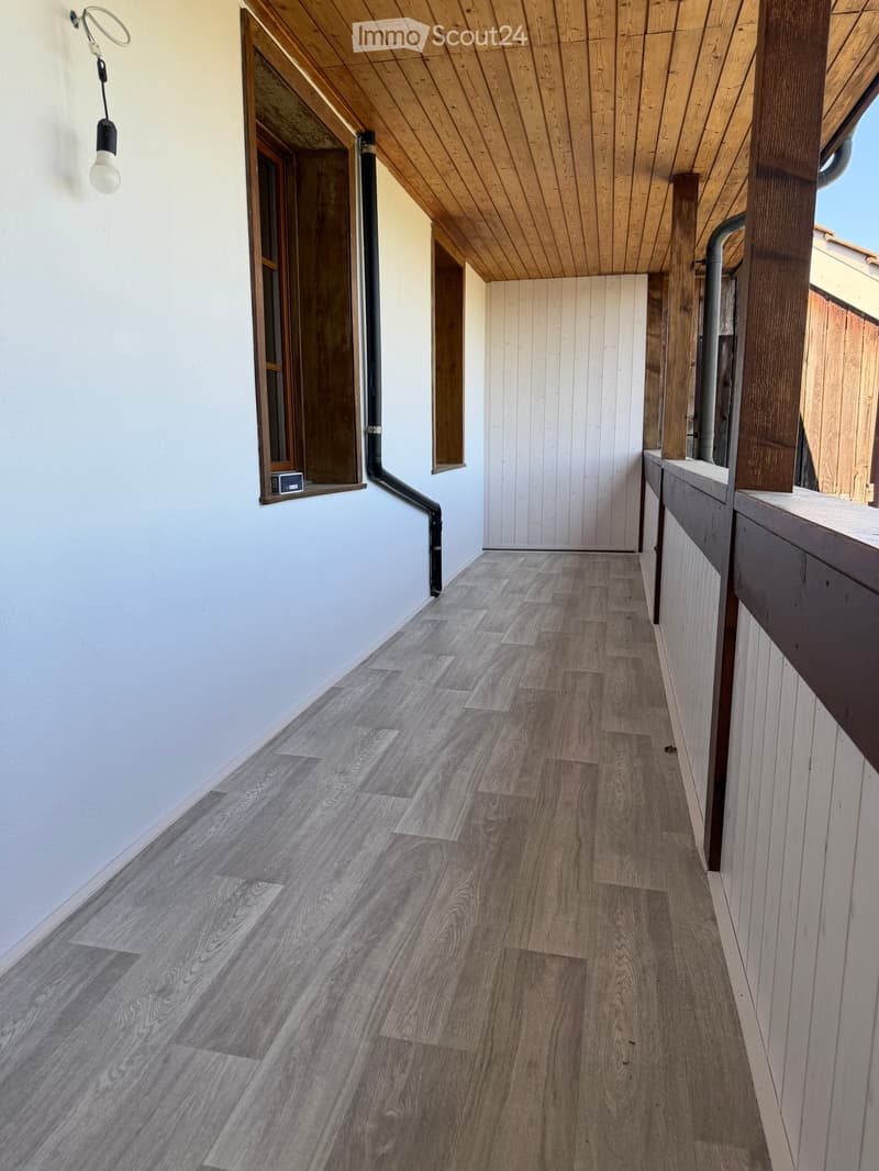 Wooden-floored hallway with white walls, wooden ceiling, and a small window on the left side.