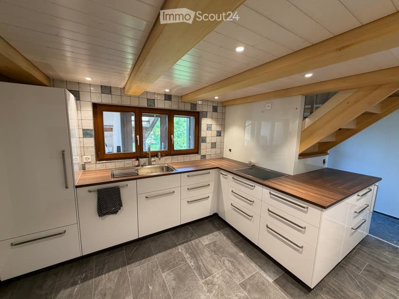 Modern kitchen with white cabinets, dark wooden countertops, stainless steel sink, and built-in stove. Features exposed wooden beams on the ceiling and large windows.