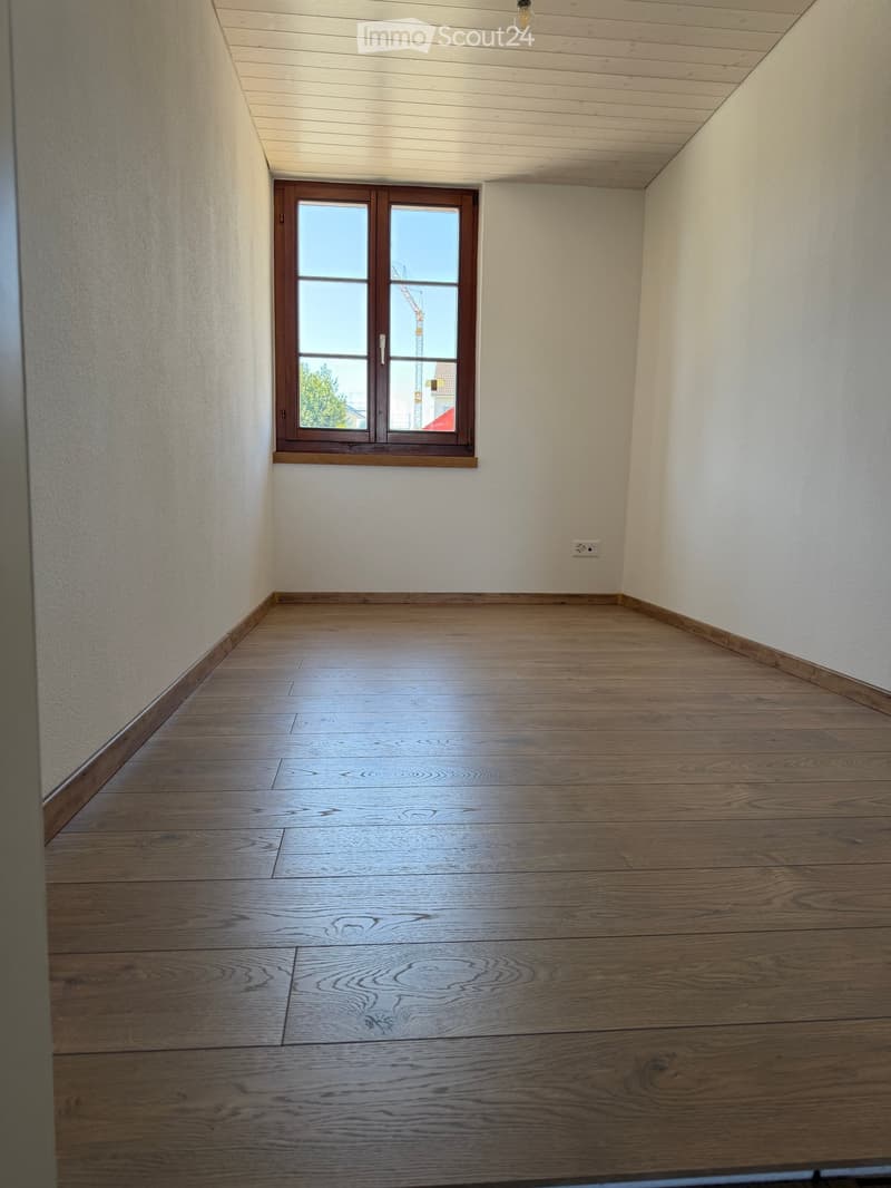 Empty room with wooden flooring, white walls, and a single window with wooden frame. No furniture or equipment present.