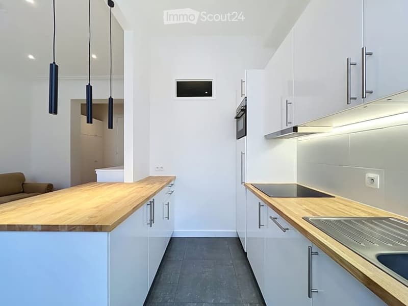 Modern kitchen with white cabinets, wooden countertops, a central island, and pendant lights. Features an oven, sink, and ample storage space.
