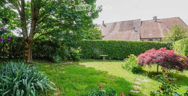 well-maintained garden with various plants, a small table, and a house in the background