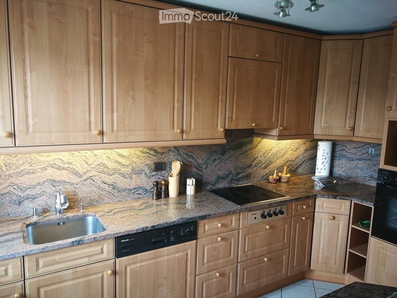 Modern kitchen with light wooden cabinets, granite countertop, stainless steel sink, dishwasher, and built-in stove and oven. Wooden utensils and spices are placed on the counter.