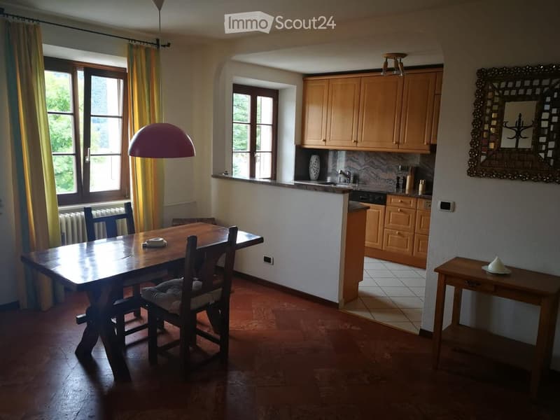 Bright kitchen and dining area with wooden dining table, chairs, cabinets, sink, and a decorative mirror.