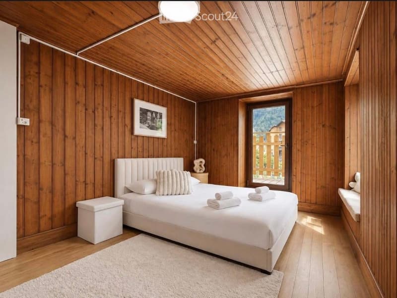 Cozy bedroom with wooden walls and ceiling, a white upholstered bed, a small bench, a picture frame, and a bench seat near the window.