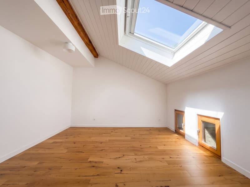 Empty room with wooden flooring, white walls, and a skylight window, featuring two wooden doors.