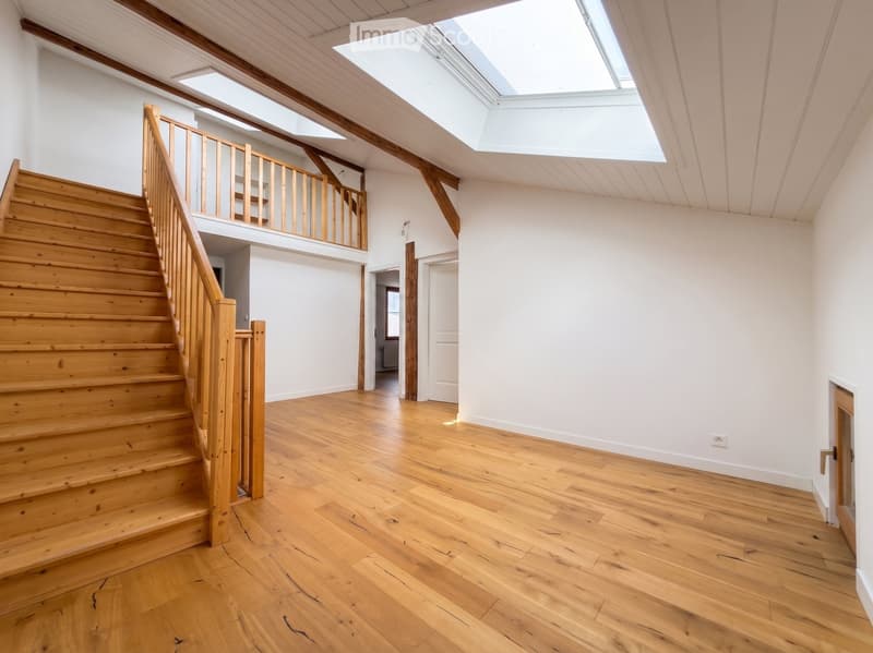 Bright, open hallway with wooden staircase leading to an upper level, wooden floors, white walls, and skylights providing natural light.