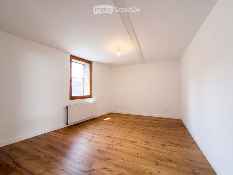 Empty room with wooden flooring, white walls, a single window with wooden frame, and a radiator below the window.