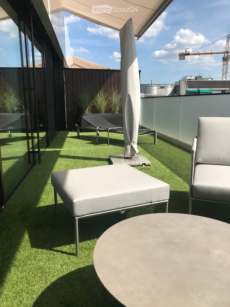 Modern rooftop terrace with artificial grass, grey sofa, chair, round table, and umbrella.