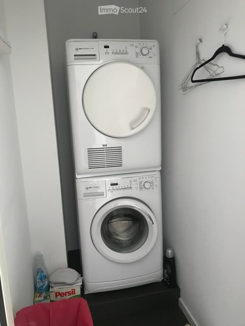 A compact bathroom with a stacked washing machine and dryer unit, a clothes hanger, and laundry supplies.