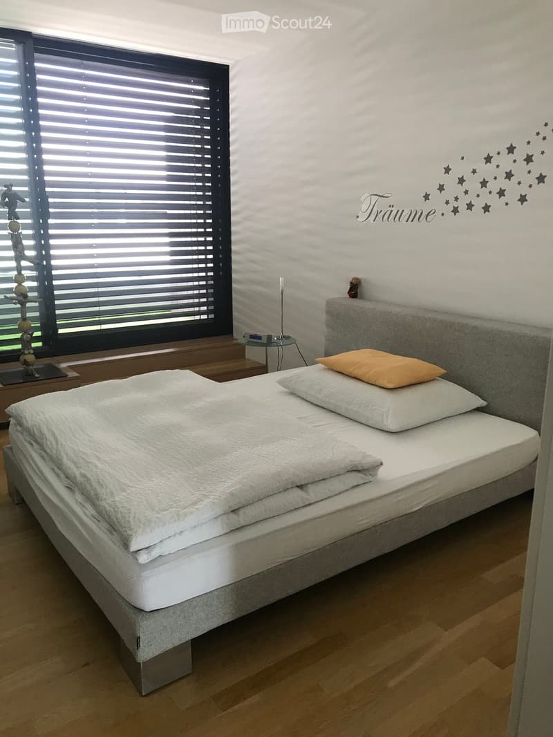 Modern bedroom with a large bed, white bedding, and a decorative wall art featuring stars and the word "Träume".