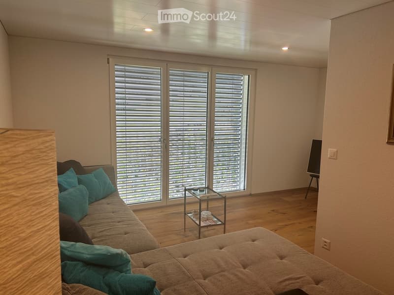 Living room with a sofa, ottoman, coffee table, and a small side table near the large sliding glass doors with blinds.