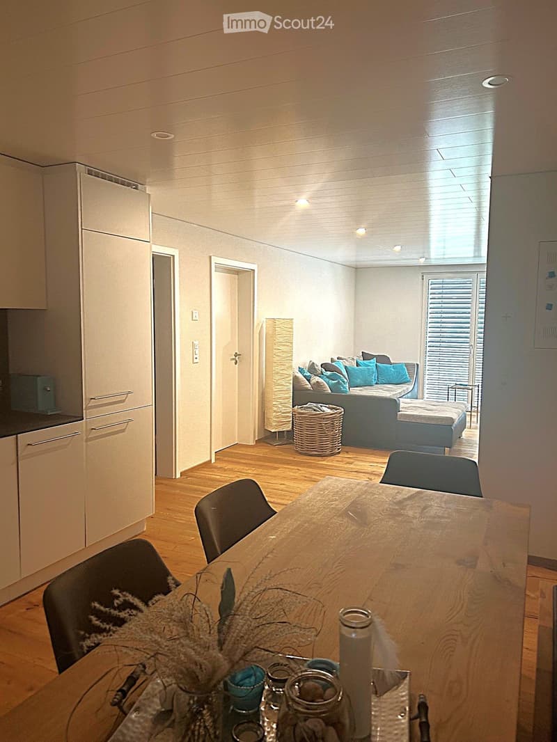 Open-plan living and dining area with modern furniture, including a sofa, dining table, chairs, and kitchen cabinets.