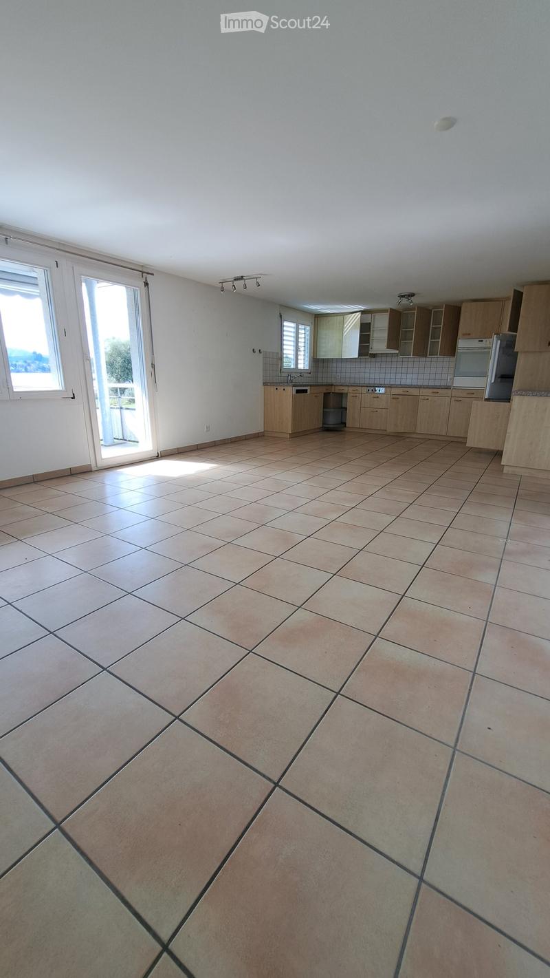 Empty kitchen with tiled floor, light wooden cabinets, and a sliding glass door leading to a balcony.