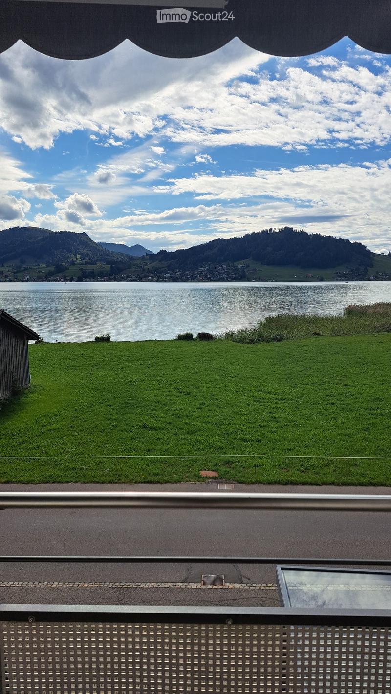 Balcony with a scenic view of a lake, green grass, and distant mountains under a partly cloudy sky.