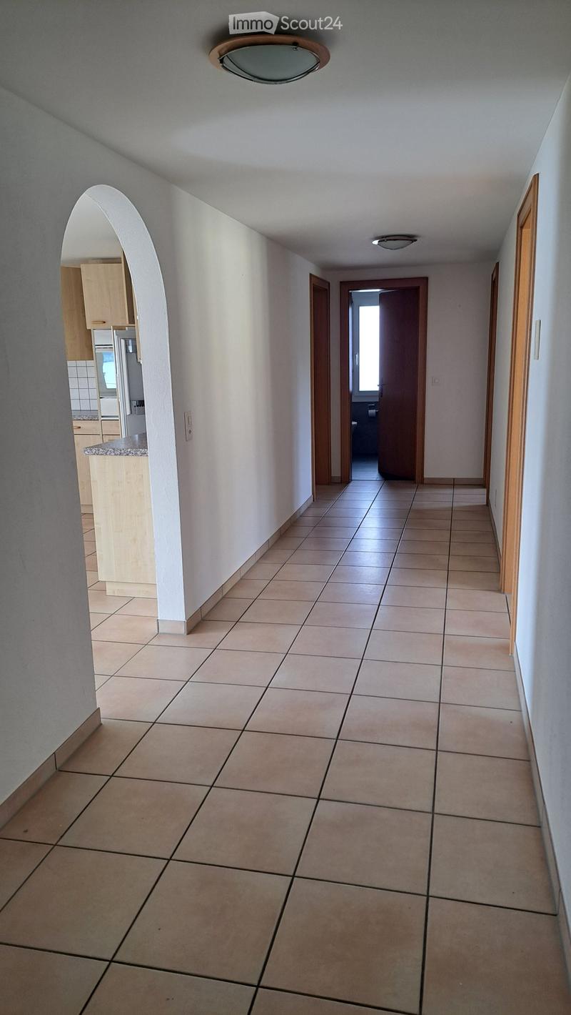 Empty hallway with tiled floor, white walls, and wooden doors leading to other rooms.