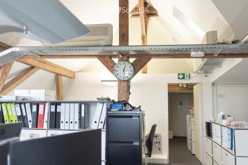 Office space with exposed wooden beams, a filing cabinet, a chair, a refrigerator, a clock, and a cabinet.