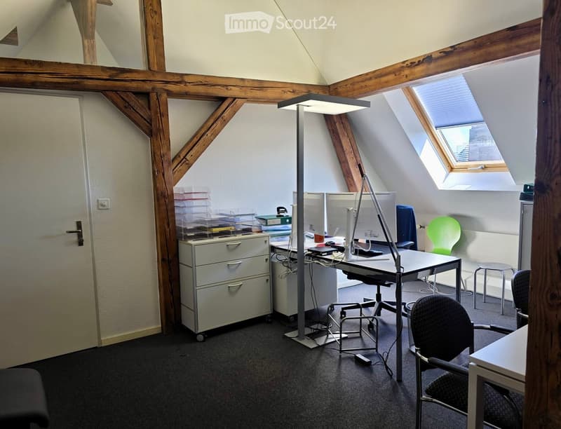 Office space with wooden beams, skylight windows, desk, chairs, and a cabinet.