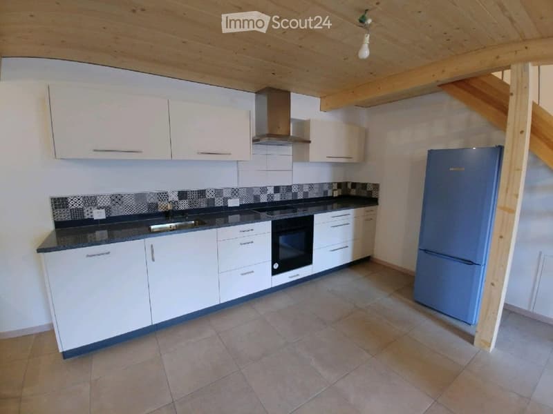 Modern kitchen with white cabinets, a dark countertop, a built-in oven, and a refrigerator. The space features a tiled backsplash and a wooden ceiling.