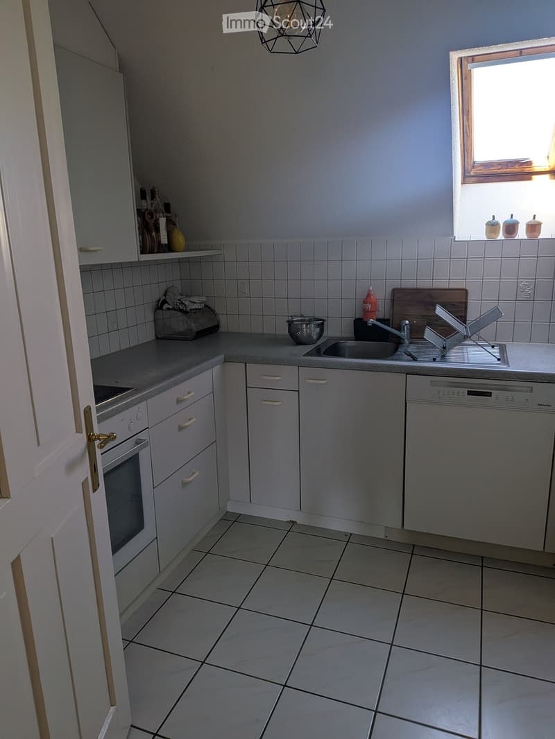 Modern kitchen with white cabinets, tiled walls, and a grey countertop. Features an oven, dishwasher, sink, and various small appliances and utensils.