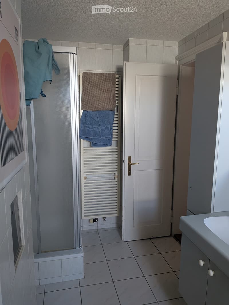 Bathroom with tiled floor, white radiator, sink, and towels hanging on the radiator and shower door.