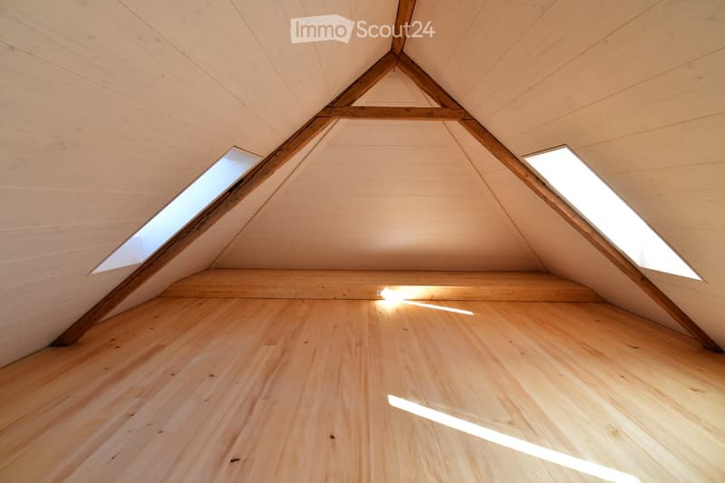 An empty attic space with wooden floors and exposed wooden beams, featuring two skylights that allow natural light to enter.