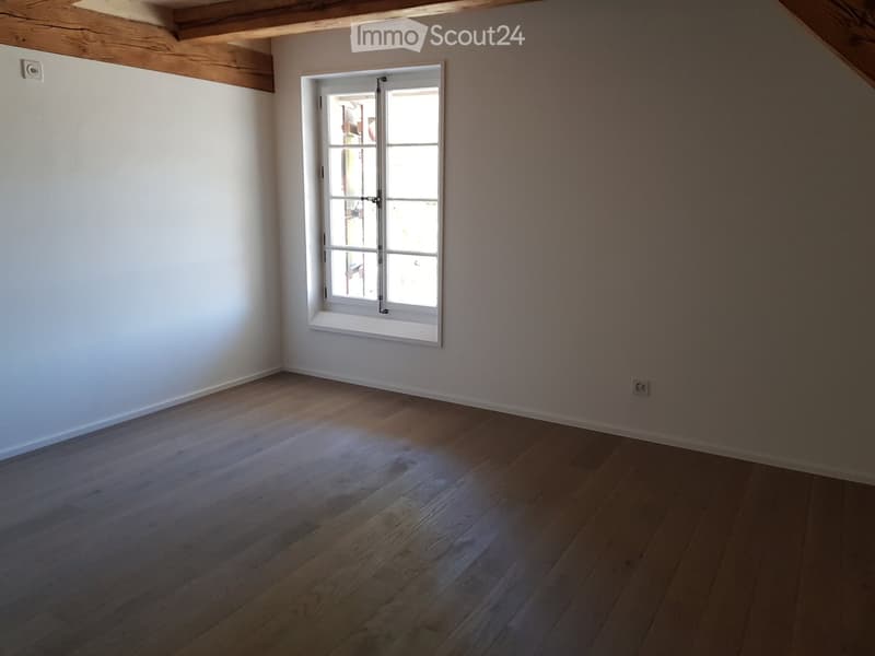 Empty room with wooden flooring and white walls, featuring a single window with white frame and multiple panes.