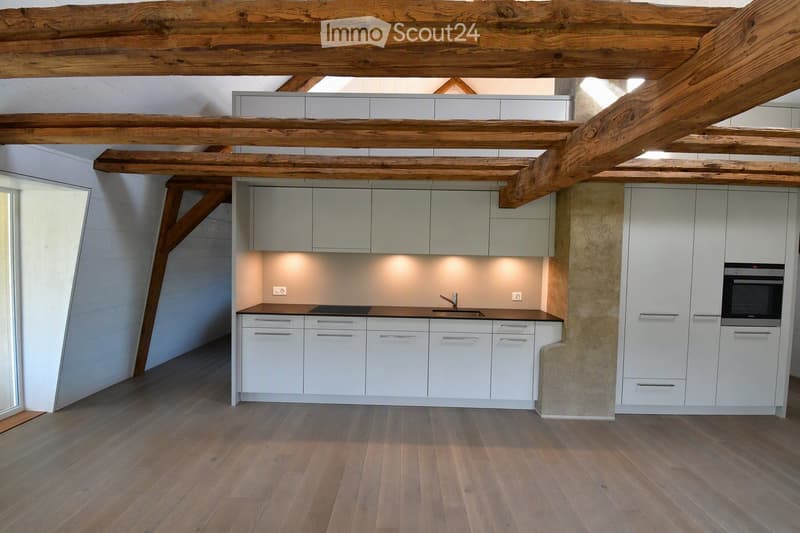 Modern kitchen with white cabinets, wooden beams, and a dark countertop.